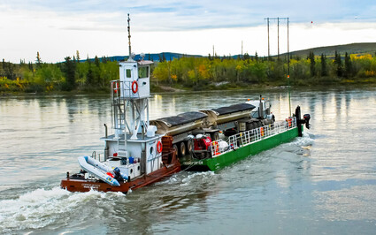 Barge carries semi with two trailers of copper concentrate across Yukon River.