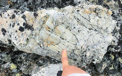 A hand pointing at a large spodumene crystal in NWT, Canada.