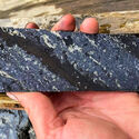 Drill core striped with metallic silver mineralization in black host rock.