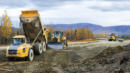 Articulating trucks, dozer, and compactor upgrade road during fall in Alaska.