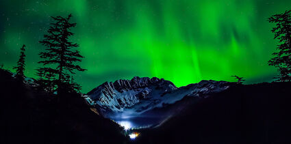 Mountain at Kensington mine silhouetted by brilliant green aurora display.