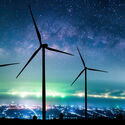 Large wind turbines silhouetted by the Milky Way and a cityscape.