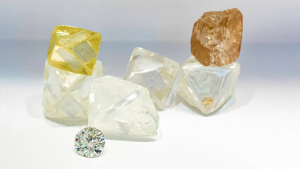 A collection of large yellow, white, and brown rough diamonds with one cut gem.