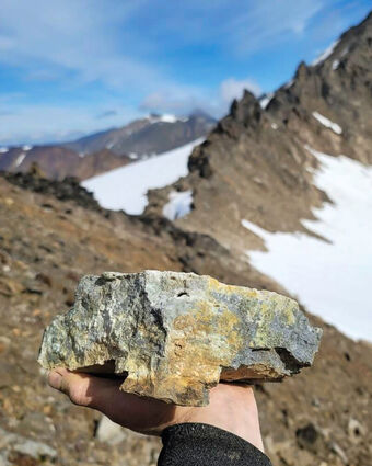 Alaska Range mountain backdrops outstretched hand holding gold-rich rock sample.