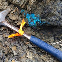 A rock hammer beside blue-colored copper mineralization in British Columbia.