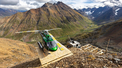 A green helicopter landed in front of orange-stained mountains at Rogue.