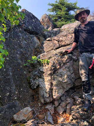 North Arrow geologist stands next to spodumene outcrop.