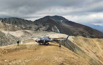 A helicopter sits on a flat mineralized area of the Alaska Range mountains.