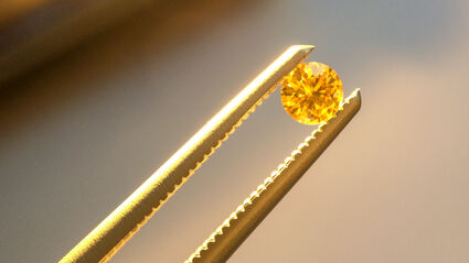 A pair of tweezers holding a fancy yellow diamond from the Naujaat project.