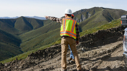 Geologists stand on slope and discuss geology of Nickel Shaw project.