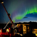 A band of purple-tinged green aurora and the big dipper above a drill rig.